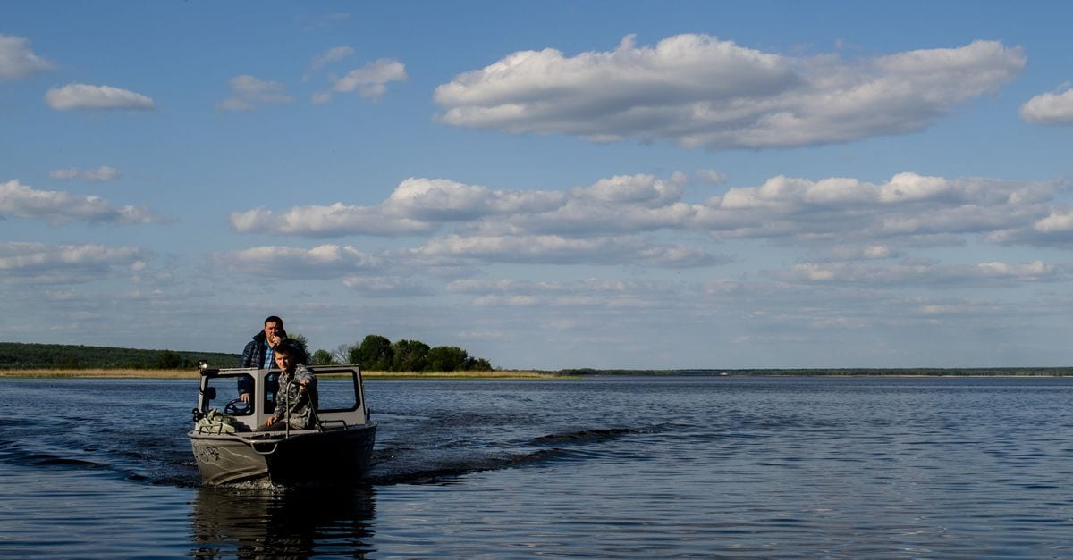 Kleines Boot mit zwei Personen gleitet bei blauem Himmel über einen weiten See